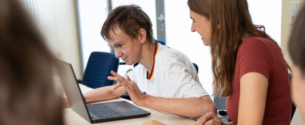 Frau zeigt Person etwas auf einem Laptop.